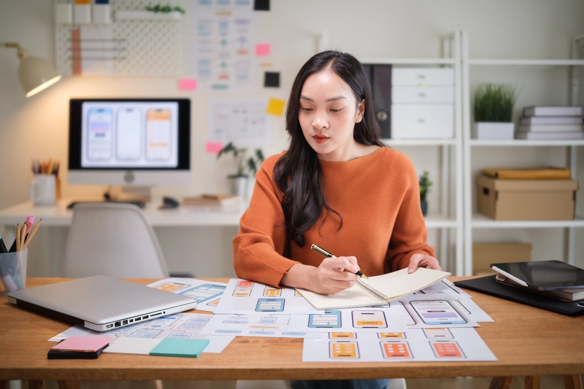 Professional UX UI designer planning user interface concepts, analyzing wireframe prototypes at a modern desk.