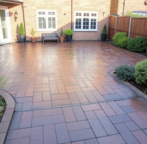 Brick patio with herringbone pattern in backyard, featuring wooden bench, potted plants, and brick house with white-framed windows
