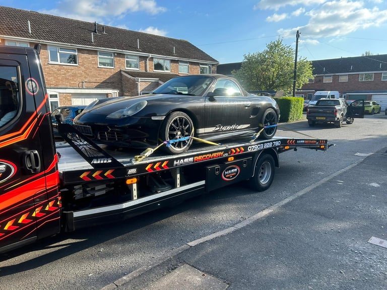 Black sports car being transported on a red and black recovery truck in a residential street