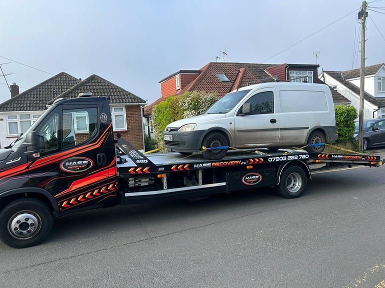 Red and black tow truck carrying a white van on a residential street with brick houses in the background