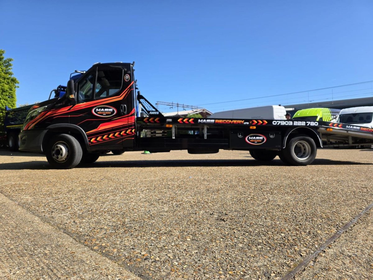 Black and red tow truck with flatbed parked on asphalt under clear blue sky